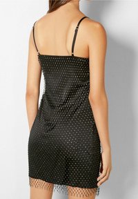 Svart satin klänning med en figurnära design, som har silvernaglad detaljer och en genomskinlig mesh-avslutning vid fållen. Justerbara spagettiband.