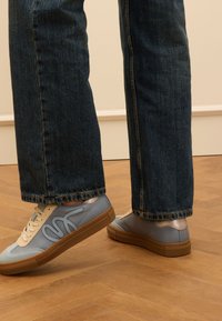 Lichtblauwe leren sneakers met beige accenten, rubberen zool en golvende motief. Draag met een donkere spijkerbroek, kort boven de enkel.