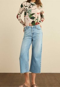 Long-sleeve floral top with a light pink base, paired with high-waisted light blue jeans featuring frayed hems and a loose, cropped shape.