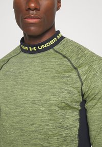 Groene sportshirt met een gestructureerde stof, zwarte accenten en een halslijn met "Under Armour" branding in het geel.