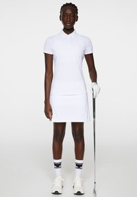 Vit polotröja och klänning kombination gjord av lättviktigt tyg. Tillbehör inkluderar en golfhandske och skor, samt randiga strumpor.