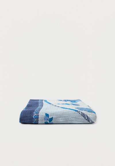 Serviette bleu clair pliée avec bordure bleu foncé et motif floral sur fond blanc uni.