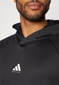 Sort atletisk hættetrøje med tekstureret stof, prydet med en karakteristisk hætteudskæring og et hvidt Adidas basketball-logo.
