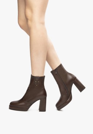 Stivali alla caviglia in pelle marrone con tacco spesso, chiusura con zip laterale, decorazione in catena e texture liscia.