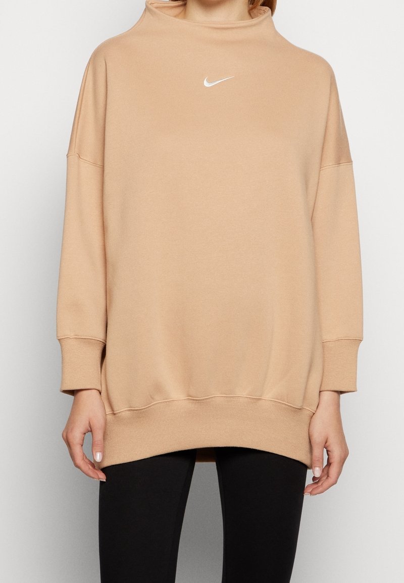 Sweatshirt beige surdimensionné avec col montant, manches longues et poignets côtelés. Présente le logo Nike blanc sur la poitrine. Tissu doux et texturé.