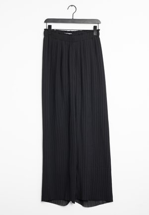 Czarne wysokie spódnice w kant z szerokimi nogawkami wiszące na czarnym wieszaku na białym tle.