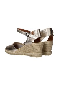 Sandalias de cuña doradas metálicas con suela estilo espadrille, que cuentan con una correa en el tobillo y una superficie texturizada. Parte del dedo suave y base de fibra natural.