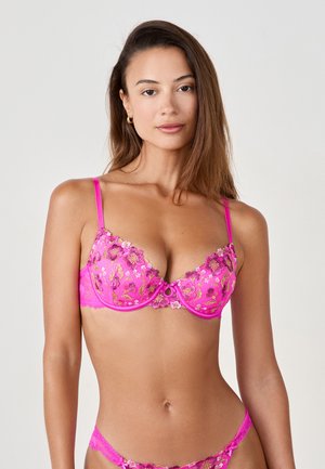 Pink lace bra with floral embroidery, semi-sheer design, underwire support, adjustable straps, and a central decorative ring.