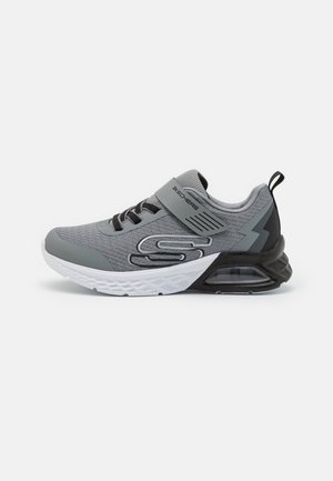 Szare buty sportowe z teksturowaną siateczką, czarnymi akcentami, regulowanym pasem oraz białą podeszwą z widoczną poduszką powietrzną.