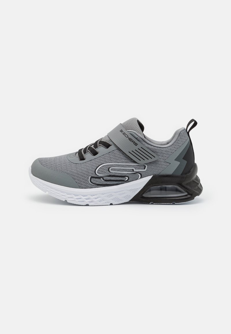 Chaussure de sport grise avec une tige en mesh texturé, des accents noirs, une sangle ajustable et une semelle blanche avec un coussin d'air visible.