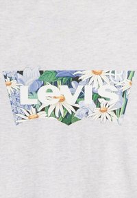 Grått tyg med en blomsterprydd Levi's-logotyp som har blå och vita blommor, prästkragar och gröna löv, avgränsad i en triangulär form.