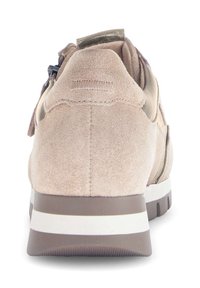 Beige suède sneaker met een gestructureerd oppervlak, bruine rubberen zool met witte strepen en een rits aan de achterkant voor gemakkelijke toegang.