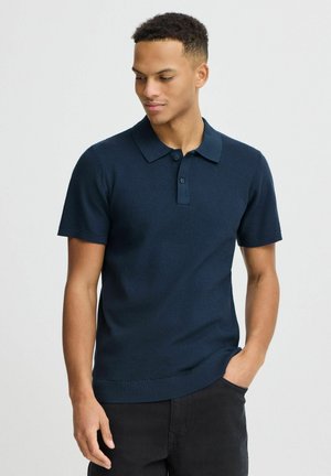 Polo en tricot bleu marine avec un col classique, un plastron à deux boutons et des manches courtes ; ourlet côtelé pour un look ajusté.