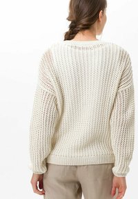 Pull en tricot couleur crème avec une coupe ample, un tissage ouvert, des épaules tombantes et des poignets et un ourlet côtelés. Matériau léger et texturé.