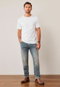 T-shirt en coton blanc, jeans délavés bleu clair, et bottines en cuir brun à la cheville. Manches courtes et col rond, coupe décontractée.