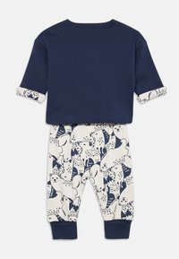 Bomulls sett bestående av en marineblå topp med rulles Slipper og kremhvite bukser prydet med marineblå dyremønstre, inkludert rever og ugler.