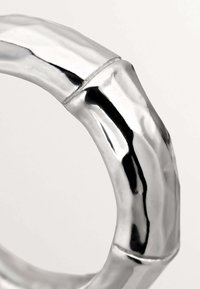 Anillo de plata con un diseño parecido al bambú, que presenta superficies suaves y reflectantes, así como una texturización sutil en las juntas.