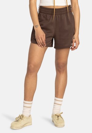 Brown athletic shorts with an elastic waistband, side pockets, and a smooth texture. Worn with cream-colored shoes and striped socks.