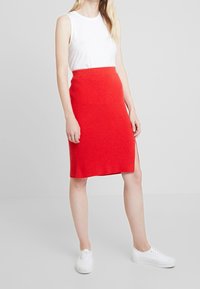 Rode geribbelde gebreide rok met een aansluitende pasvorm en een zijsplit, gecombineerd met een witte mouwloze top en witte sneakers.