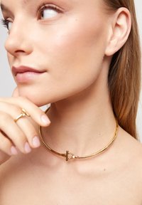 Collar choker de color dorado con forma redonda y acabado texturizado. Cuenta con un cierre de palanca con un pequeño detalle decorativo.