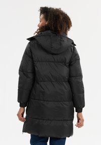 Svart vadderad jacka med huva, med en quiltad design, elastiska ärmslut och en medellång längd. Slät textur och dold dragkedja.