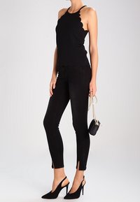 Musta, aaltoilevilla reunoilla varustettu toppi yhdistettynä mustiin, sivuleikkauksilla varustettuihin kapeisiin farkkuihin. Malli käyttää mustia, kärjellisiä korkokenkiä ja kantaa pientä laukkua.