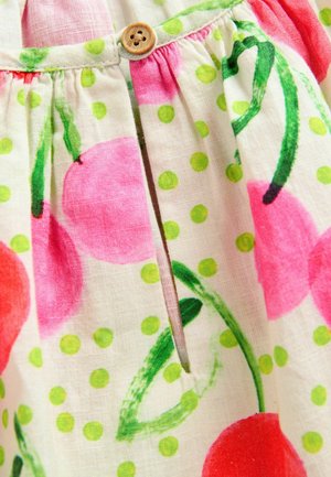 Bílá tkanina s růžovým vzorem třešní a zelenými puntíky; má nařasený pas s akcentem knoflíku poblíž malého rozparku.