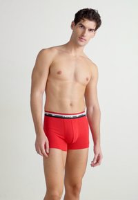 Rote Baumwollboxershorts mit einem schwarzen elastischen Bund, der das Nike-Logo trägt. Eng anliegendes Design mit glatter Textur und ohne sichtbare Muster.