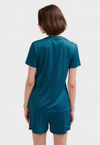 Set med sporttop och shorts i blågrönt, tillverkat i mjukt, lätt tyg. Har korta ärmar och en avslappnad passform utan synlig logotyp.