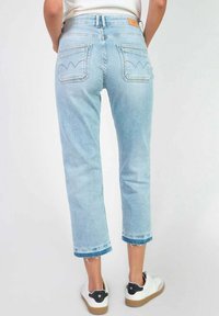 Jean en denim bleu clair avec un design cropped, comportant deux poches arrière et un ourlet effiloché. Associé à des baskets blanches.