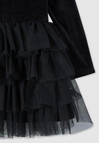 Abito nero con un corpino in corduroy texture, strati di ruffles trasparenti all'orlo e una fodera liscia sotto.