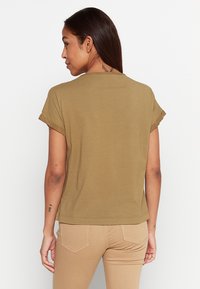 Koszulka bawełniana w kolorze oliwkowym z krótkim rękawem, z podwiniętymi mankietami i luźnym krojem. Z ty�łu znajduje się wykończenie szyi przeszyciem oraz gładka faktura.