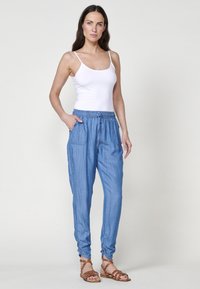 Pantaloni jogger azzurri chiari, comodi e larghi, con vita elasticizzata, due tasche laterali e polsini arricciati. Abbinati a una canotta bianca e sandali.
