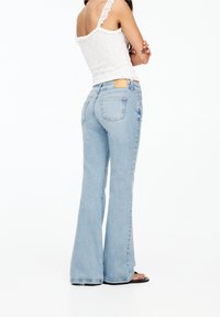 Jeans a vita alta, di un blu chiaro, a gamba svasata, realizzati in denim, con cinque tasche e un’etichetta in pelle marrone sulla parte posteriore della vita.