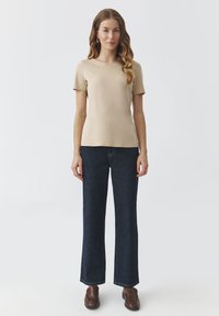 Haut beige à manches courtes associé à un jean large bleu foncé. Le tissu semble lisse ; le haut présente un col rond et une coupe décontractée.