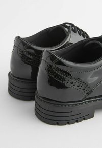 Chaussures en cuir verni noir avec un bout arrondi, des détails perforés et une semelle en caoutchouc texturée. Design profil bas avec un système de laçage.