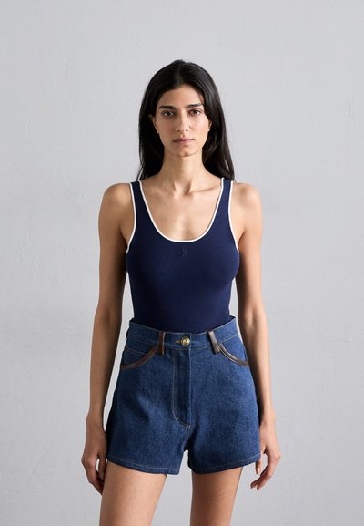 Body navy cu tiv alb, asortat cu pantaloni scurți din denim cu talie înaltă. Pantalonii scurți au închidere cu nasture și accente maronii la buzunare.