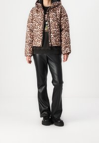 Pikowana kurtka w panterkę z kapturem, zapinana na zamek błyskawiczny z prążkowanymi mankietami. Połączona z czarnymi spodniami z sztucznej skóry i solidnymi czarnymi butami.