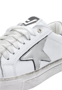 White leather sneaker featuring a silver star detail, textured laces, and a grey outsole with a slightly worn effect.