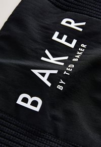 Mustast kangast, millel on julged valged kirjaviisid "BAKER" ja "by TED BAKER". Tekstuur näib sile ning ülaservas on soonilised aktsendid.