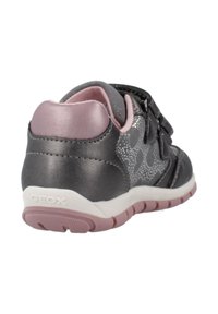Zapatilla gris con acentos rosas, que presenta un upper texturizado, dos correas de velcro y una suela de goma con un patrón de trazado.
