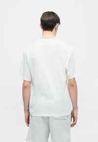 Λευκό βαμβακερό t-shirt με κοντά μανίκια, στρογγυλή λαιμόκοψη και άνετη εφαρμογή, φορεμένο με γκρι σορτς. Απλός σχεδιασμός, χωρίς σχέδια ή γραφικά.