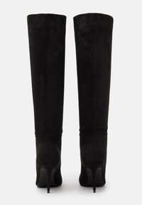 Bottes montantes en daim noir avec un bout pointu et un talon stiletto fin, présentant une texture lisse et un design minimaliste.