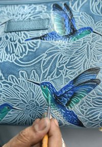 Blaue Lederaccessoires mit handgemalten Kolibris und aufwendigen floralen Designs. Der Künstler malt Details mit einem feinen Pinsel.