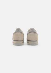 Beżowe zamszowe sneakersy z teksturowaną szaro-sietkową nakładką, o zaokrąglonym kształcie i subtelnym nadrukowanym logo na pięcie. Neutralna gumowa podeszwa.
