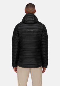 Zwarte pufferjack met capuchon, met horizontale stiksels, een gladde textuur en het "MAMMUT"-logo op de bovenrug.