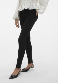 Jeans elásticos negros con un corte ajustado, que presentan una textura suave y una cintura alta. Combinados con tacones slingback negros de punta afilada.