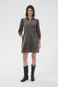 Abito in velluto a righe grigio con zip frontale, collo a camicia e maniche a tre quarti. Il modello indossa stivali cowboy neri. Sfondo minimalista.