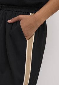 Svarta byxor med elastisk midja, utrustade med en ficka och en beige sidremsa kantad med krämfärgad. Slätt tyg med avslappnad passform.