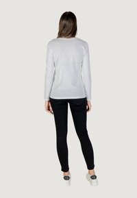 Top bianco a maniche lunghe e pantaloni neri slim-fit. Il top ha un collo rotondo; i pantaloni presentano tasche e una texture liscia.